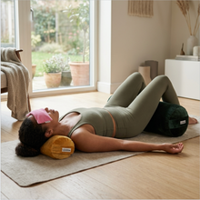 A collection of colorful velvet yoga bolsters in pink, blue, and yellow, designed to support various body parts.